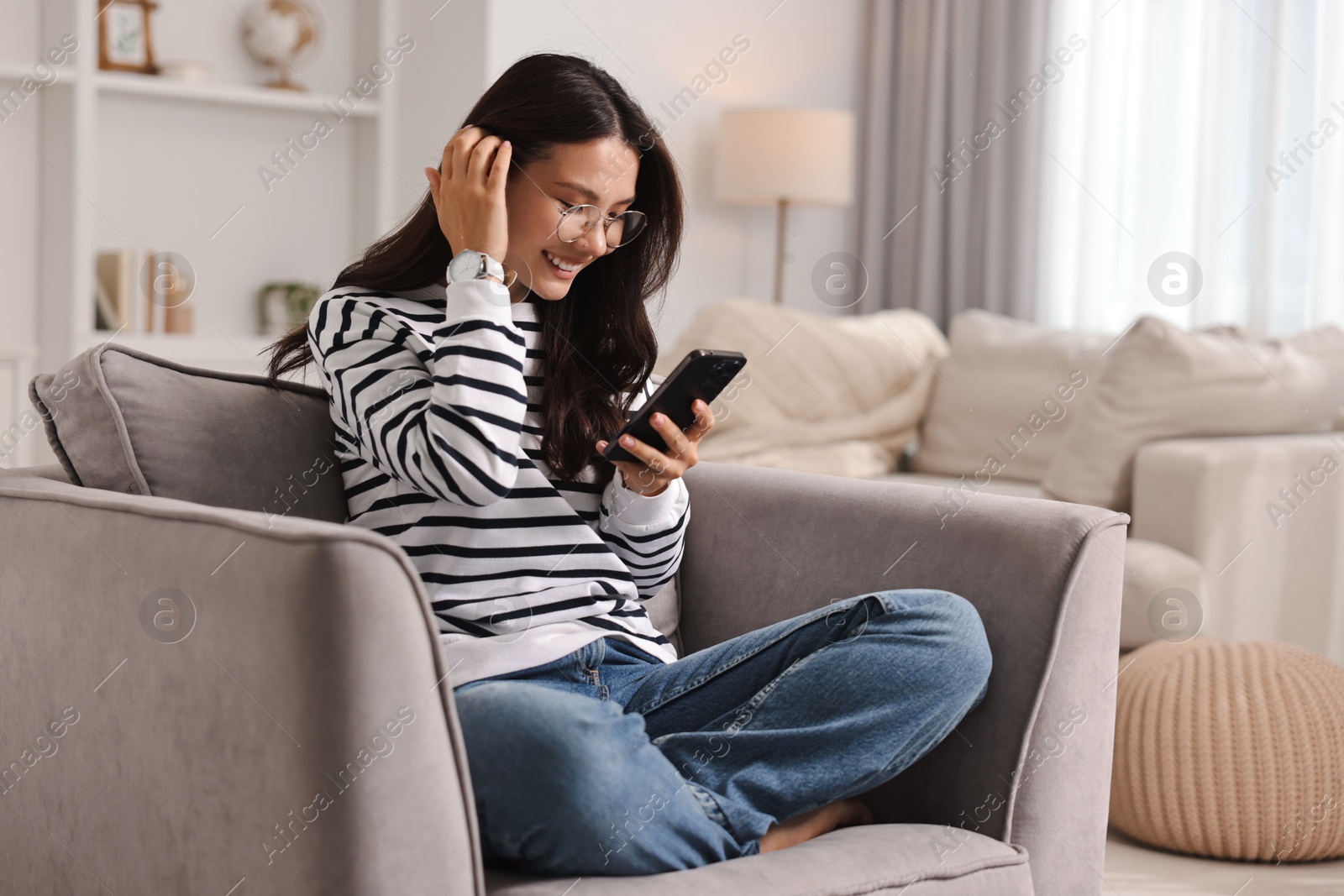 Photo of Smiling woman with smartphone on armchair at home