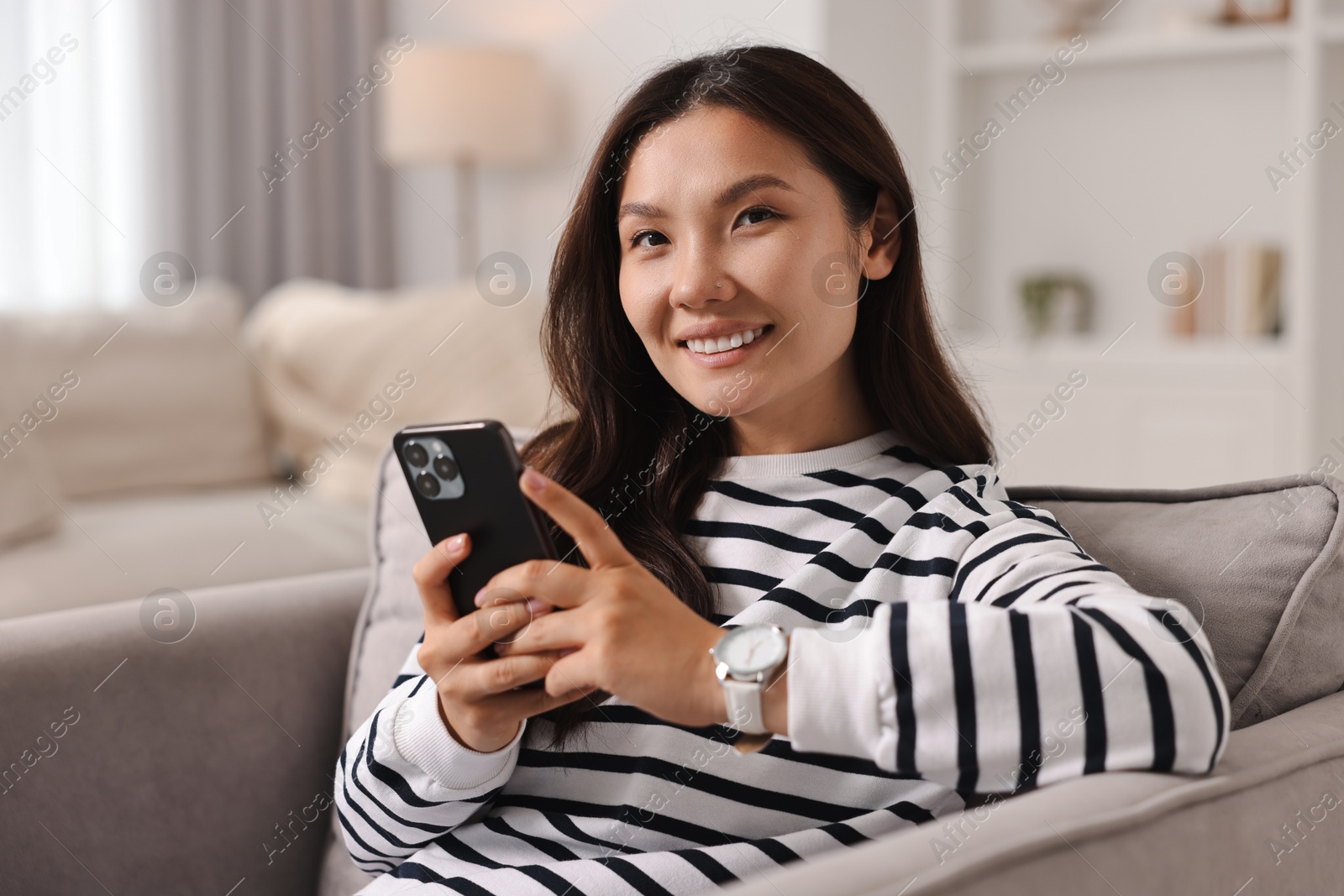 Photo of Smiling woman with smartphone on armchair at home