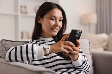 Photo of Smiling woman with smartphone on armchair at home