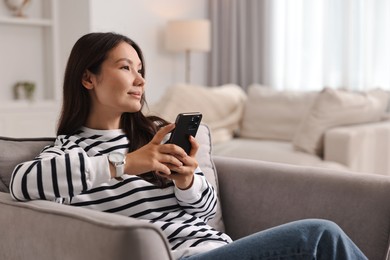 Photo of Beautiful woman with smartphone on armchair at home