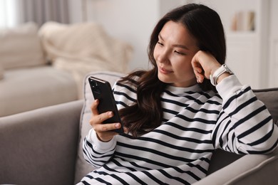 Photo of Beautiful woman with smartphone on armchair at home