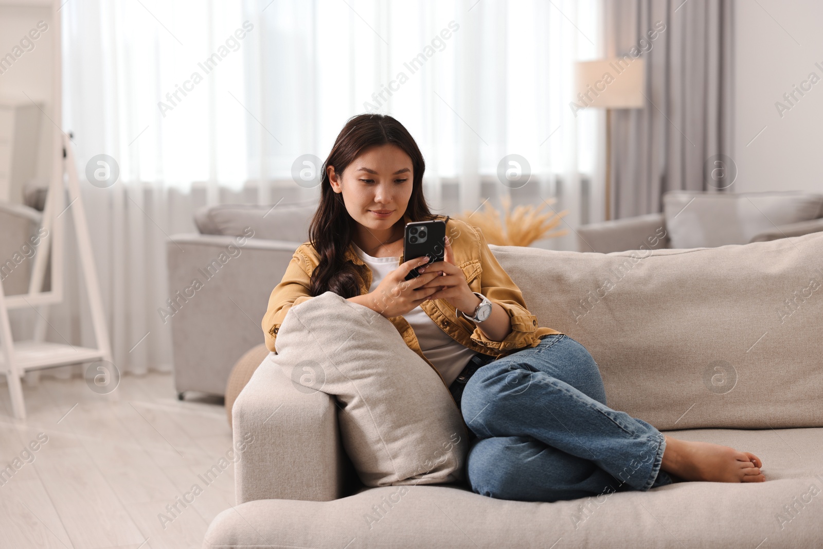 Photo of Beautiful woman with smartphone on sofa at home