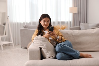 Beautiful woman with smartphone on sofa at home