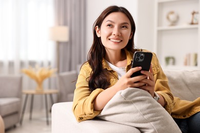 Smiling woman with smartphone at home. Space for text