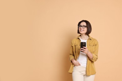 Smiling woman with smartphone on beige background. Space for text