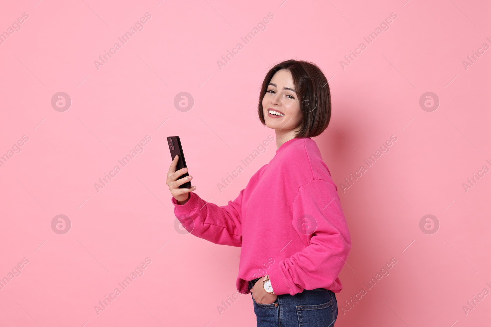 Photo of Smiling woman with smartphone on pink background