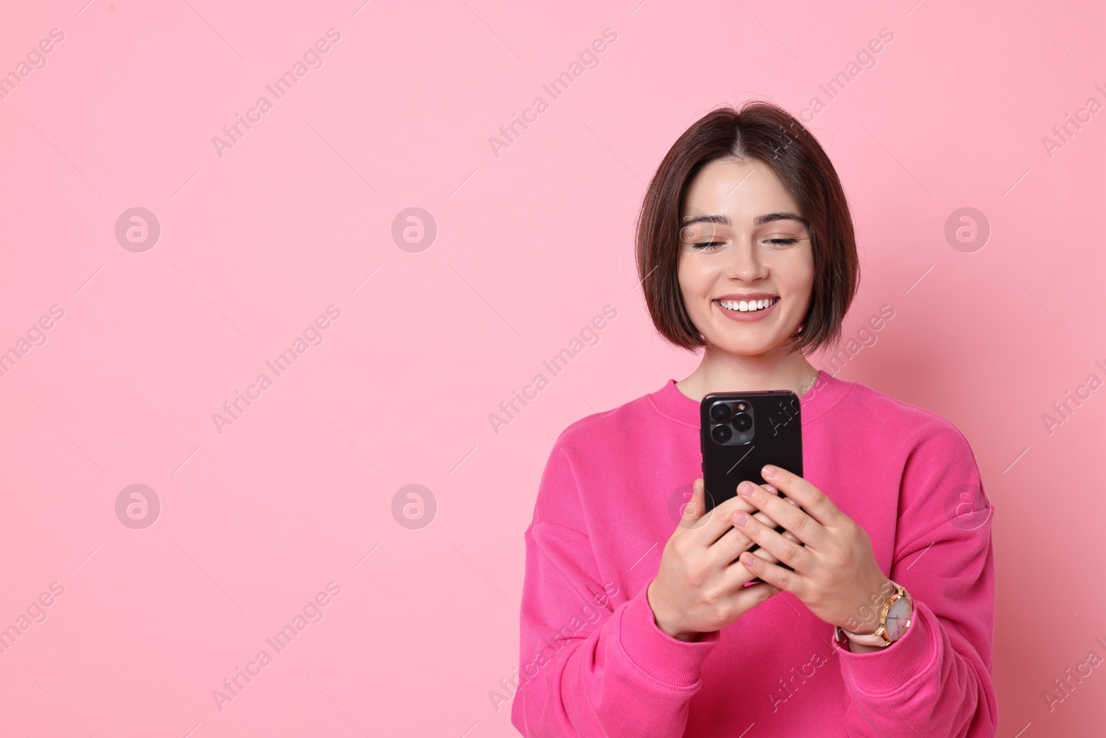 Photo of Smiling woman with smartphone on pink background. Space for text