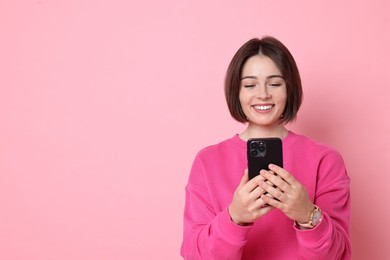 Photo of Smiling woman with smartphone on pink background. Space for text