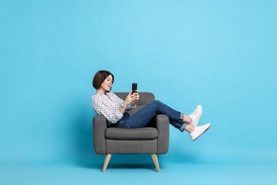 Photo of Smiling woman with smartphone resting on armchair against light blue background