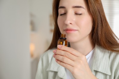 Woman with bottle of essential oil at home, space for text