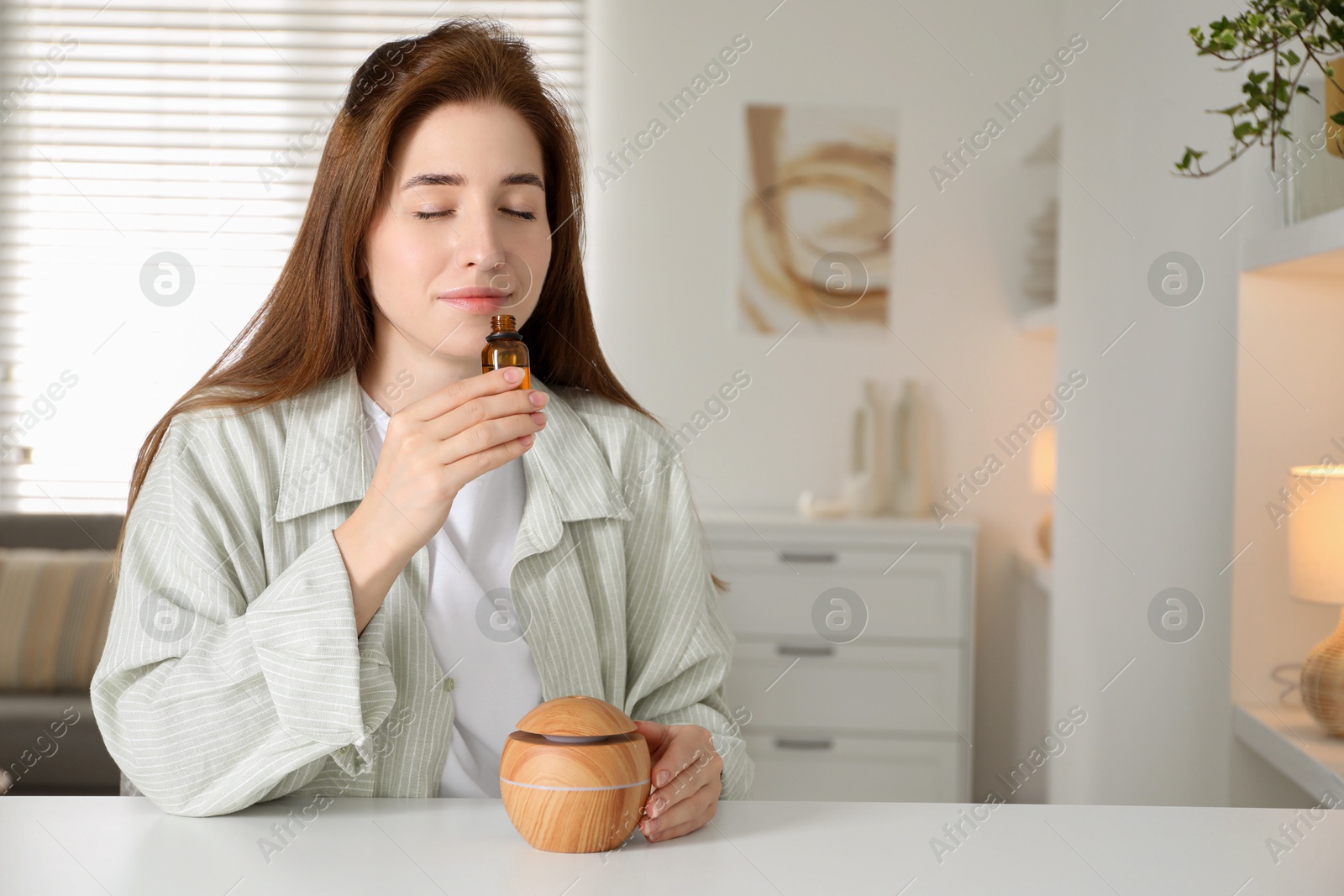 Photo of Woman with aroma diffuser and bottle of essential oil at home