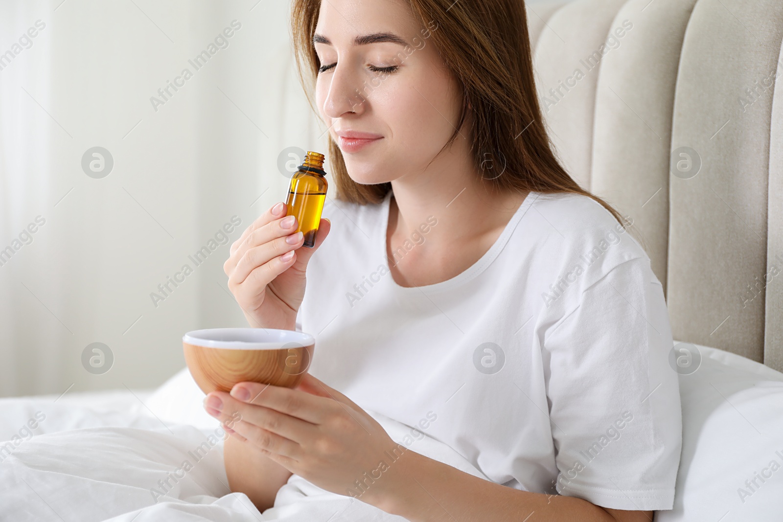 Photo of Woman with aroma diffuser and bottle of essential oil at home