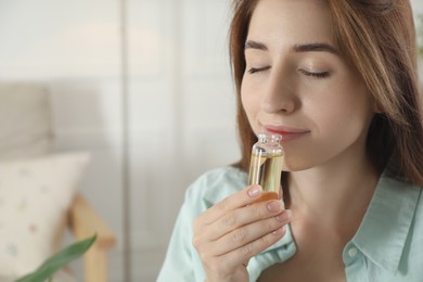 Photo of Woman with bottle of essential oil at home, space for text