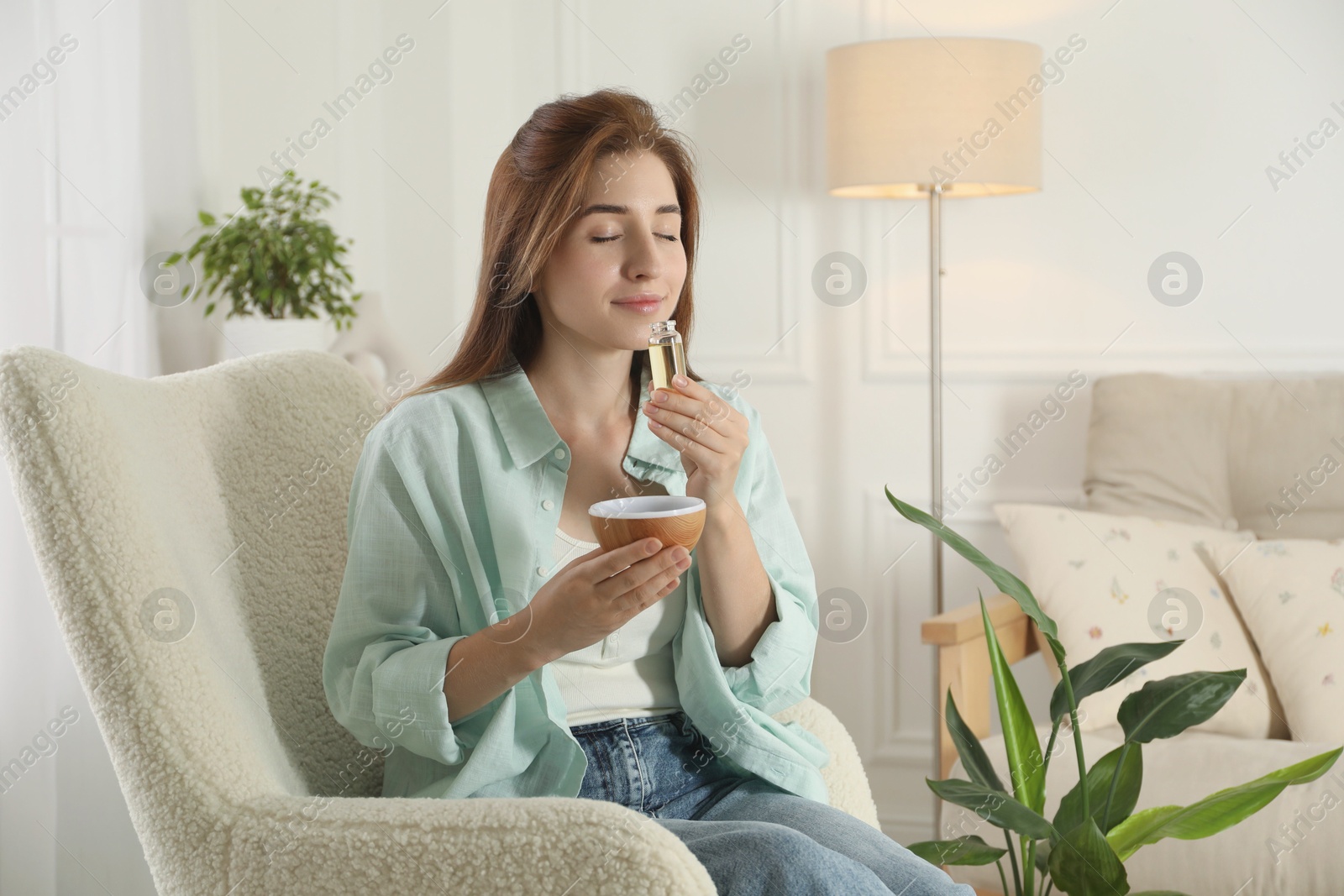 Photo of Woman with aroma diffuser and bottle of essential oil at home