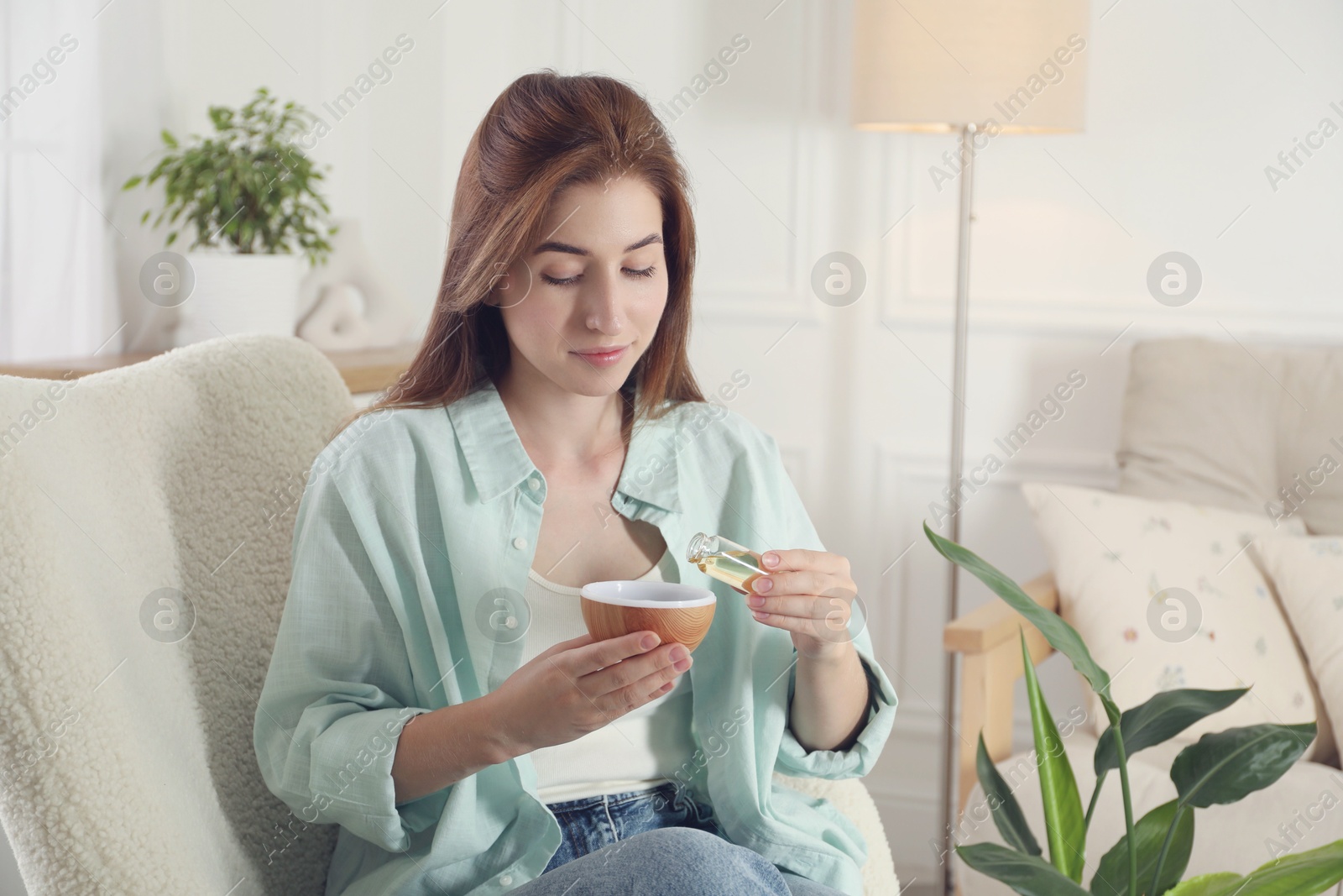 Photo of Woman adding essential oil to aroma diffuser at home