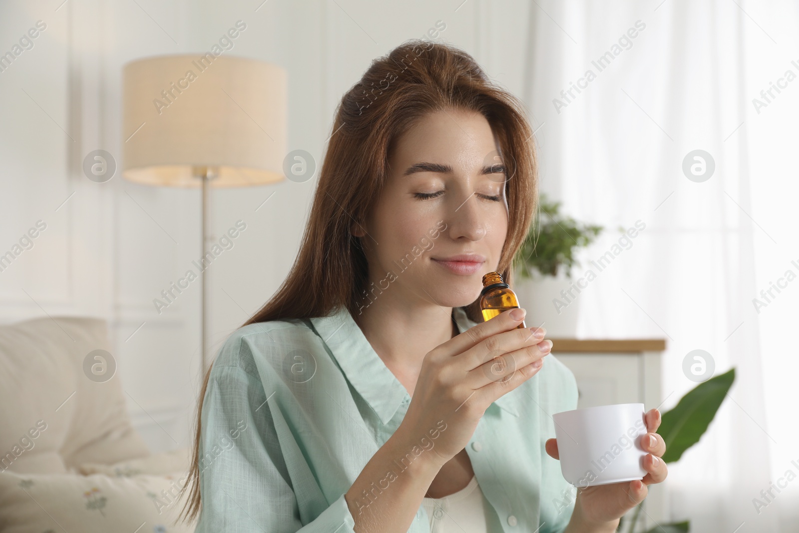 Photo of Woman with aroma diffuser and bottle of essential oil at home