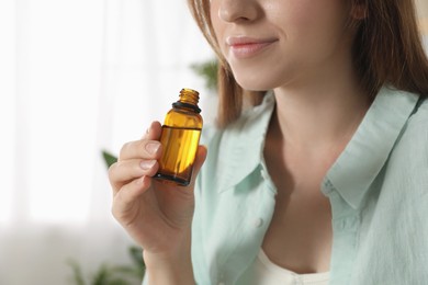 Photo of Woman with bottle of essential oil at home, closeup