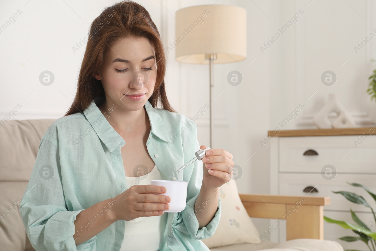 Photo of Woman adding essential oil to aroma diffuser at home