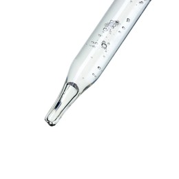 Dripping cosmetic serum from pipette on white background