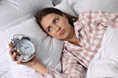 Sleepy woman with alarm clock in bed at lunch time