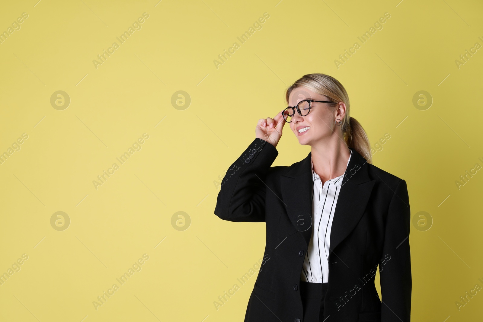 Photo of Beautiful woman in stylish black suit on yellow background, space for text