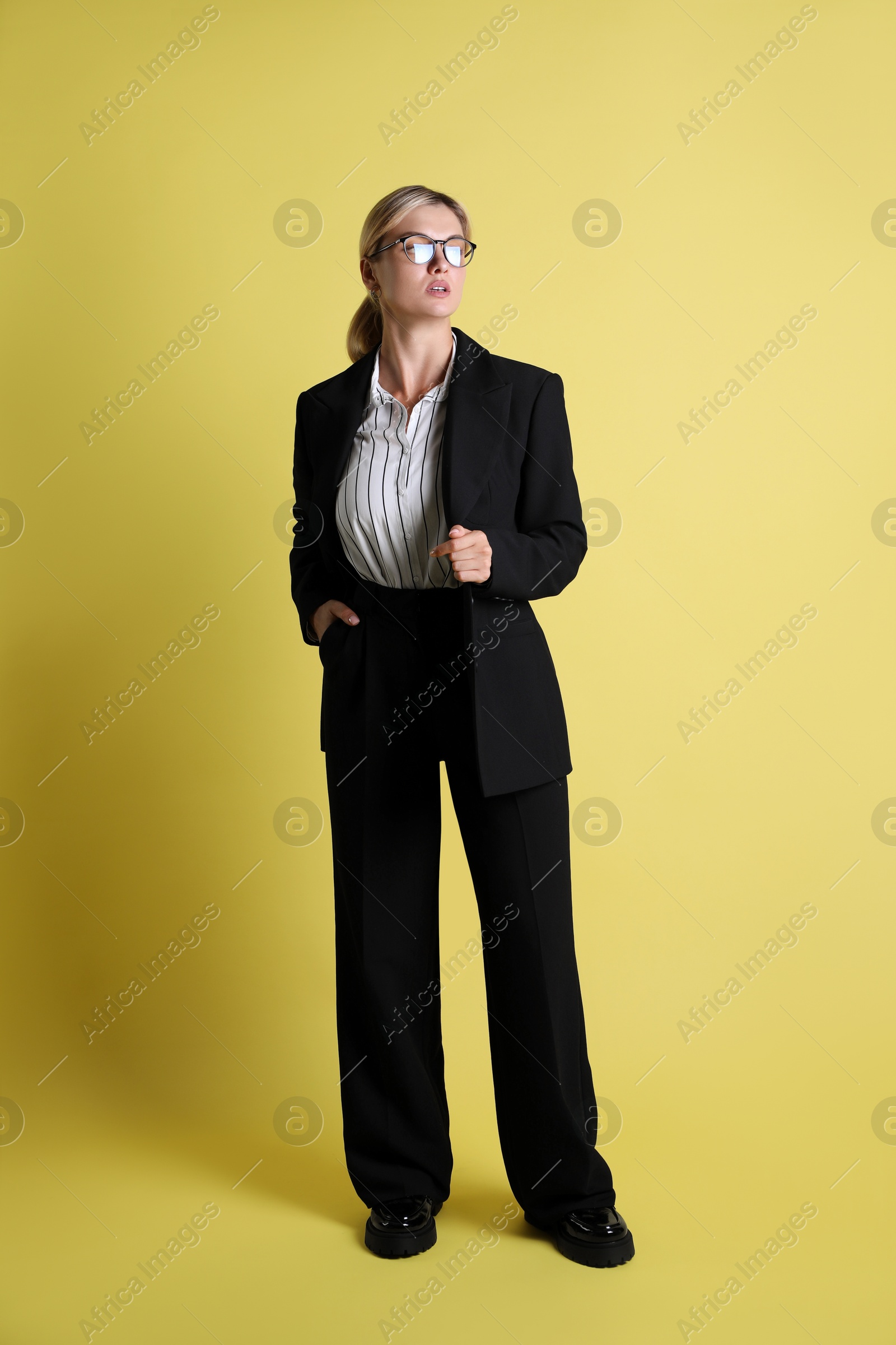 Photo of Beautiful woman in stylish black suit on yellow background