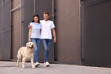 Happy couple walking with cute Golden Retriever dog outdoors, low angle view. Space for text