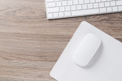 Photo of Computer mouse with mousepad and keyboard on wooden desk, top view. Space for text