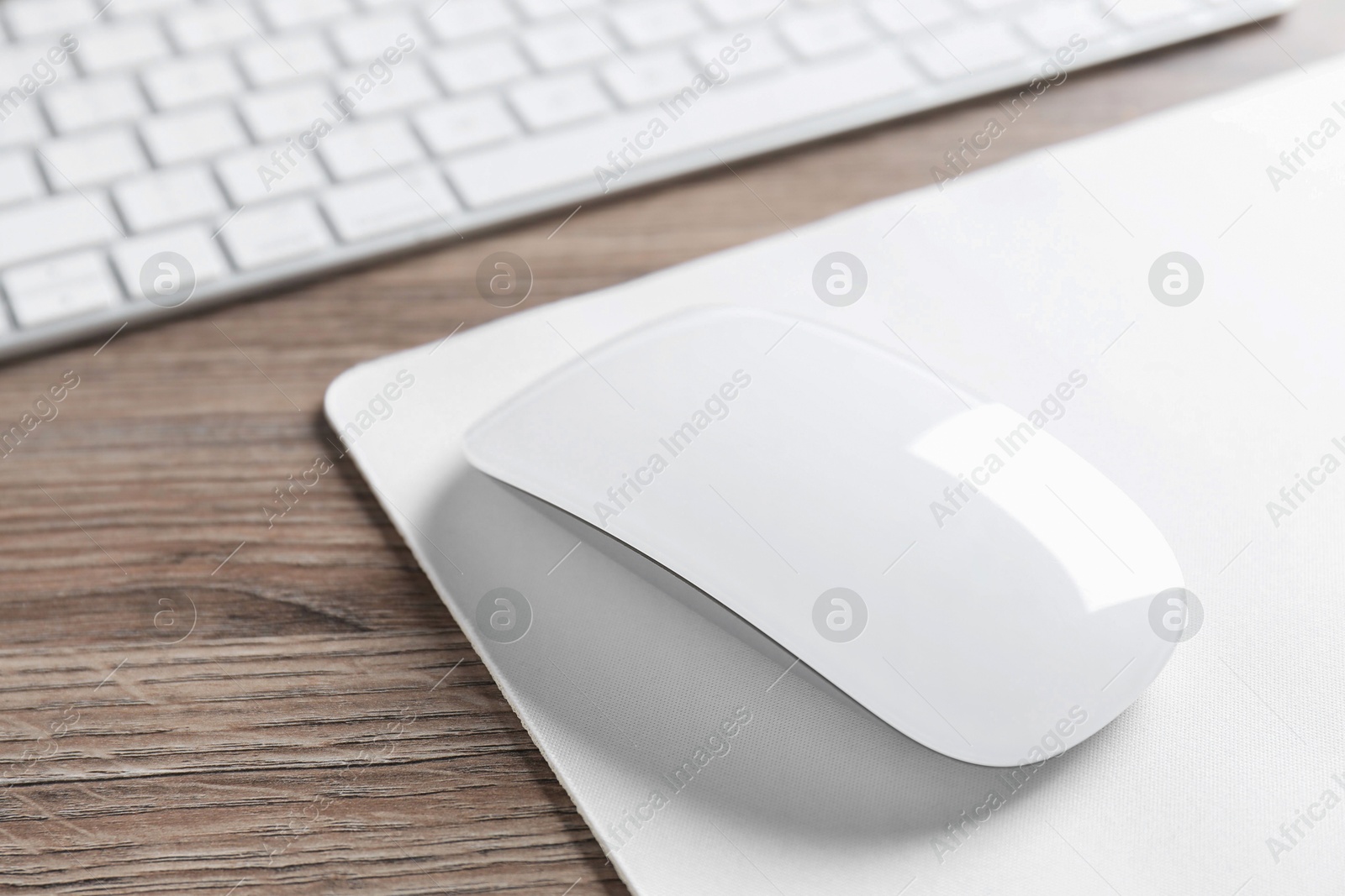 Photo of Computer mouse with mousepad and keyboard on wooden desk, closeup