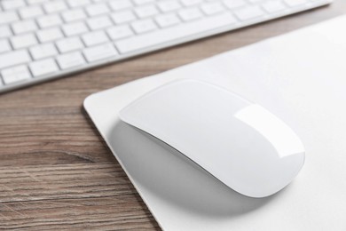 Photo of Computer mouse with mousepad and keyboard on wooden desk, closeup