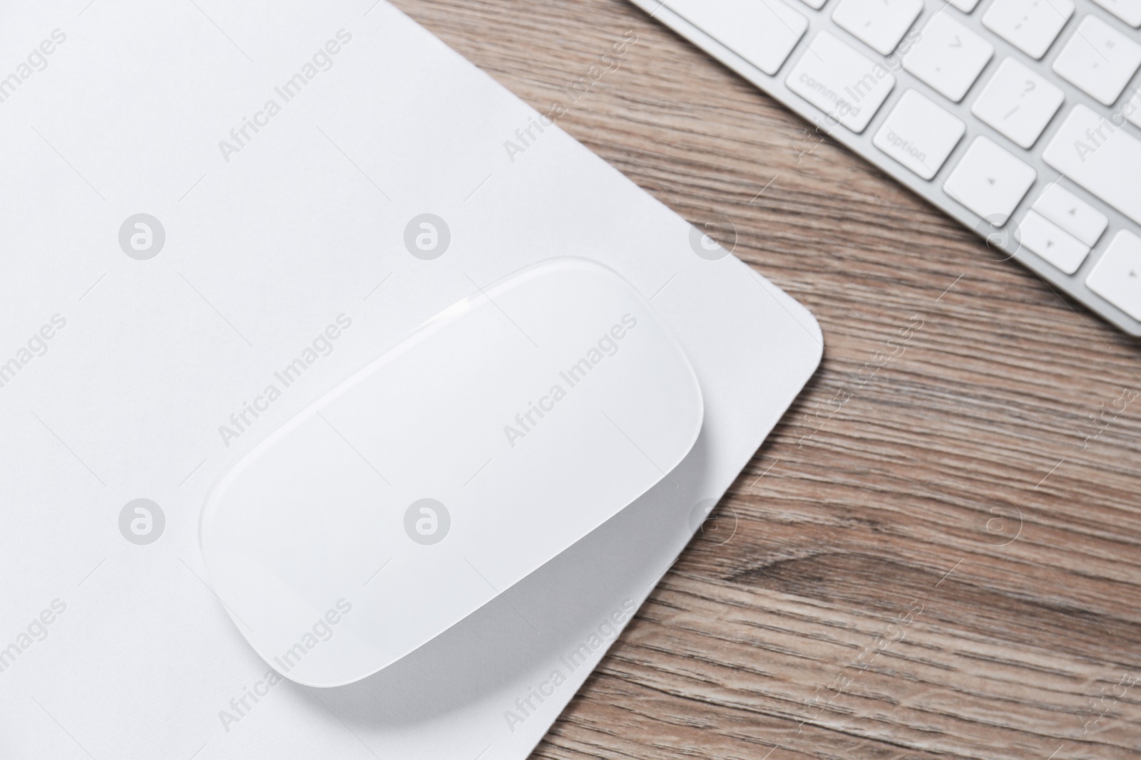 Photo of Computer mouse with mousepad and keyboard on wooden desk, top view