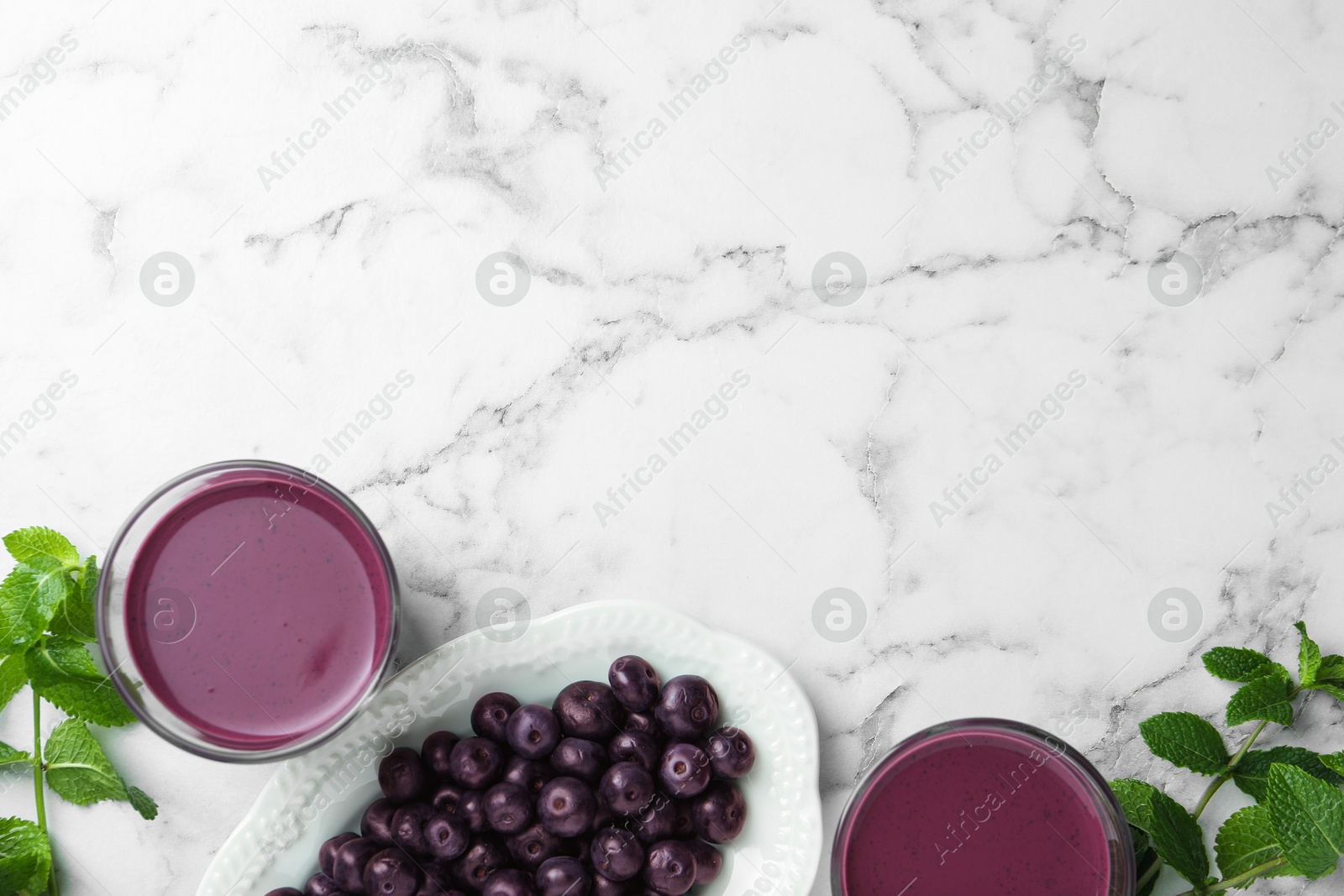 Photo of Tasty fresh acai juice in glasses, mint and berries on white marble table, flat lay. Space for text