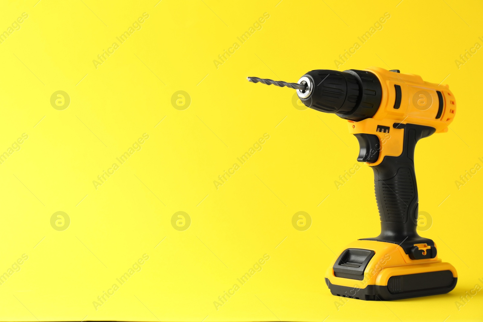 Photo of Modern cordless electric drill on yellow background. Space for text