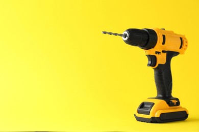 Photo of Modern cordless electric drill on yellow background. Space for text