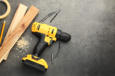 Modern cordless electric drill, sawdust, planks and bits on grey table, flat lay