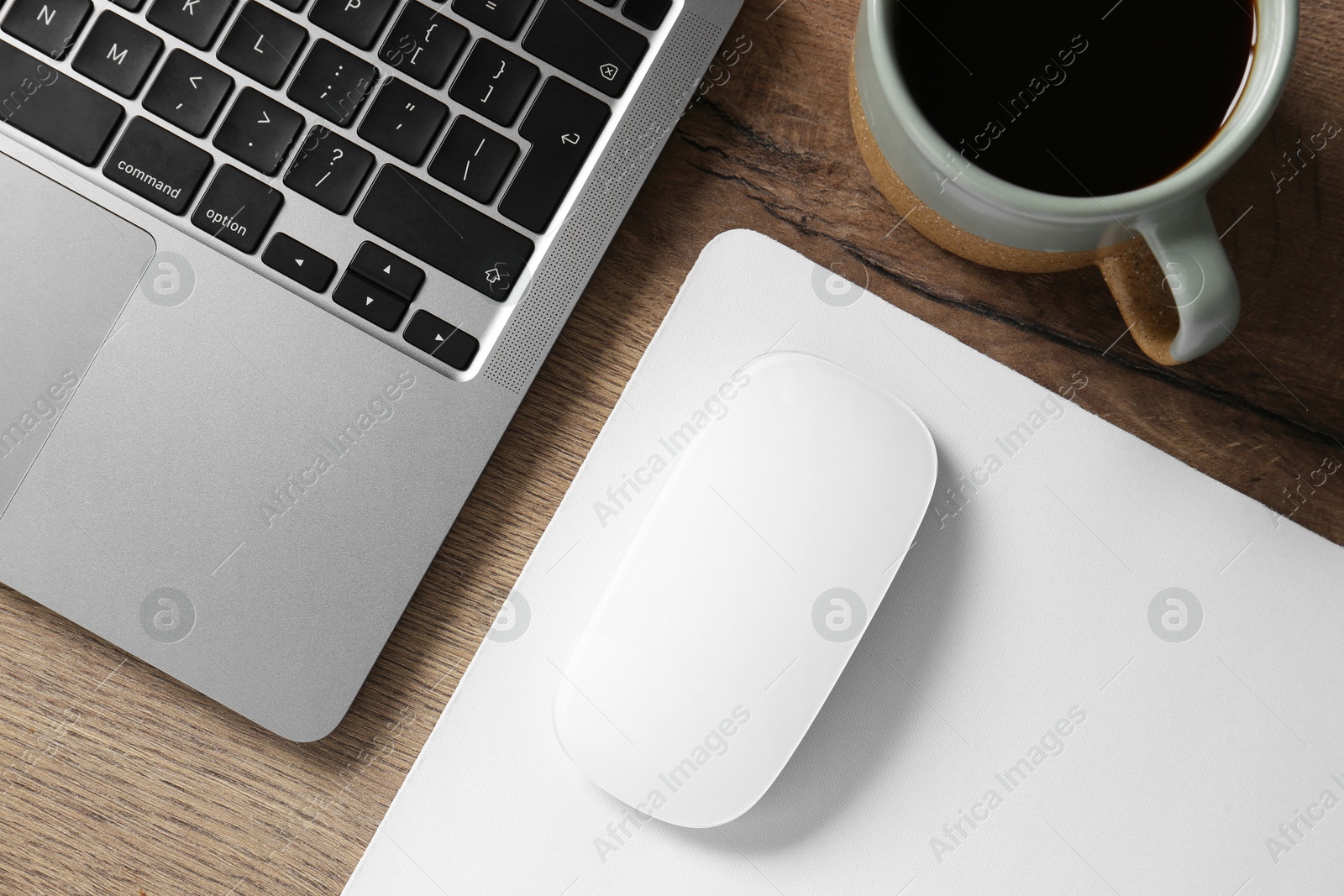 Photo of Computer mouse with mousepad, cup of coffee and laptop on wooden table, flat lay