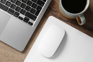 Photo of Computer mouse with mousepad, cup of coffee and laptop on wooden table, flat lay