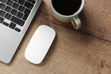 Photo of Computer mouse, cup of coffee and laptop on wooden table, flat lay