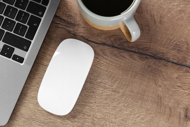 Photo of Computer mouse, cup of coffee and laptop on wooden table, flat lay