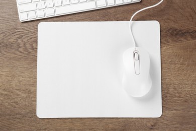 Photo of Computer mouse with mousepad and keyboard on wooden table, flat lay