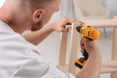 Photo of Man with electric screwdriver assembling furniture in room, closeup