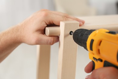 Photo of Man with electric screwdriver assembling furniture in room, closeup