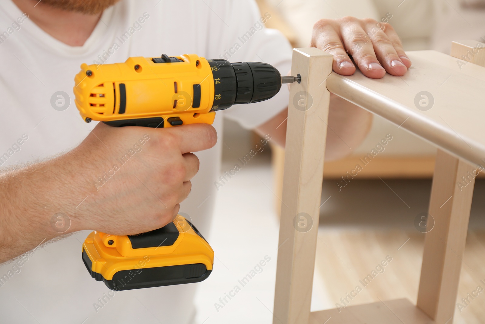 Photo of Man with electric screwdriver assembling furniture in room, closeup