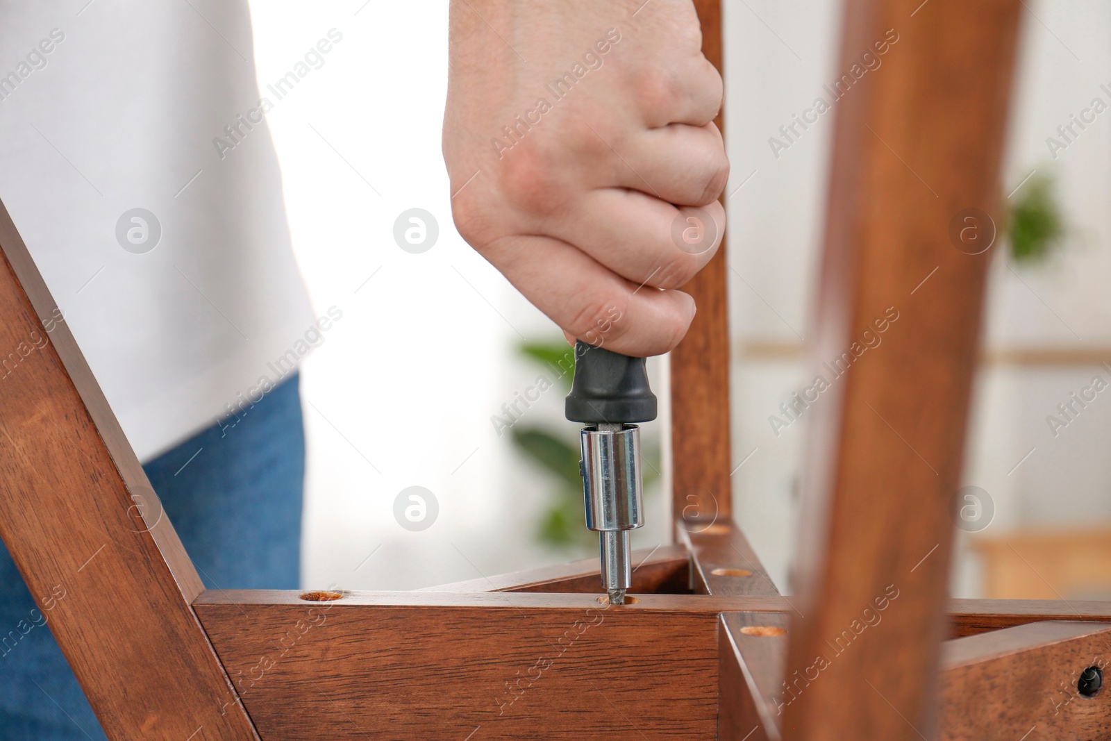 Photo of Man with screwdriver assembling furniture indoors, closeup