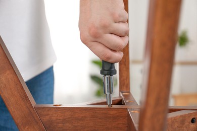 Photo of Man with screwdriver assembling furniture indoors, closeup