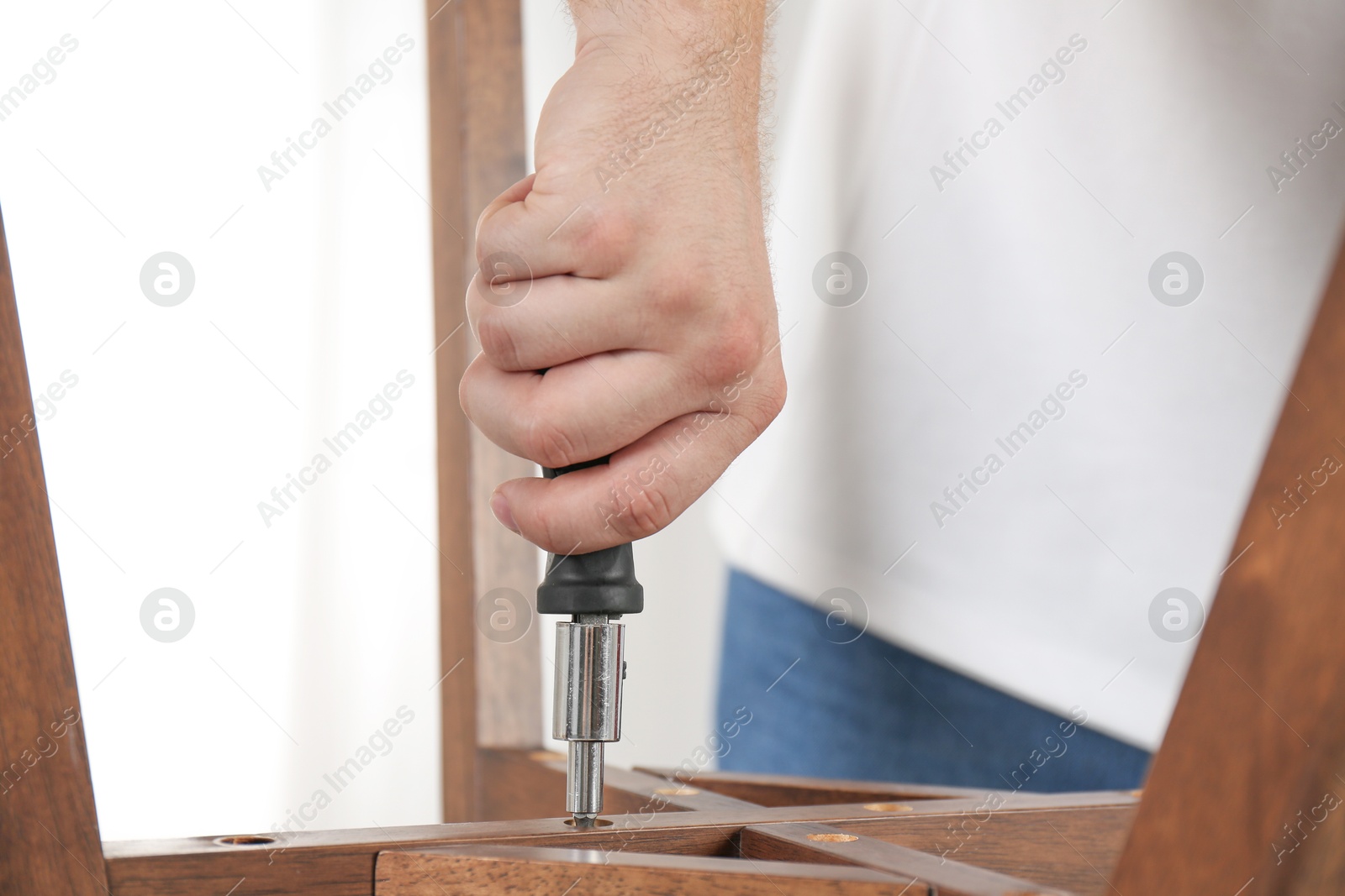 Photo of Man with screwdriver assembling furniture indoors, closeup