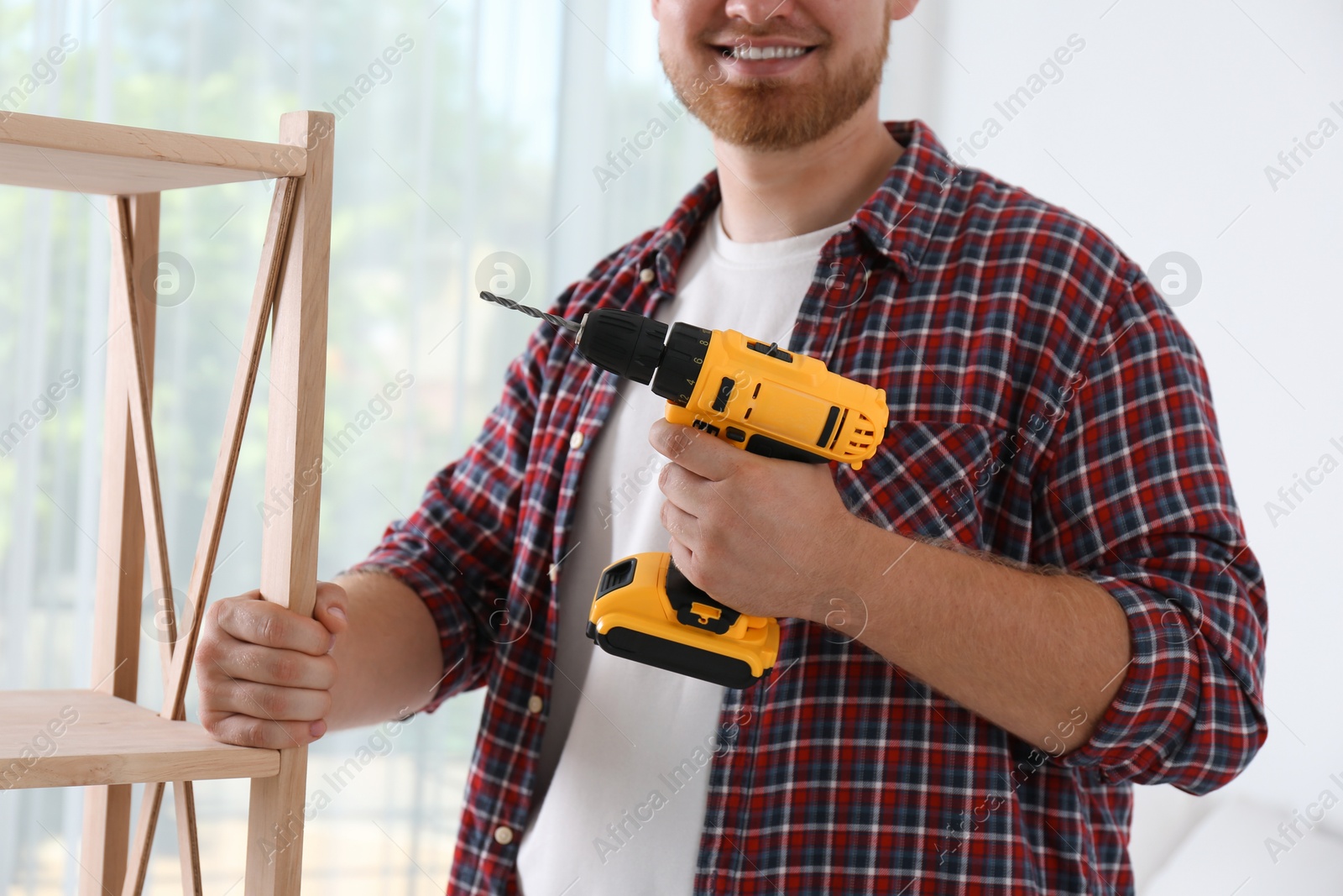 Photo of Man with electric screwdriver at home, closeup. Assembling furniture