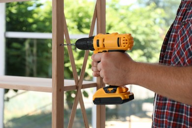 Photo of Man with electric screwdriver assembling furniture indoors, closeup