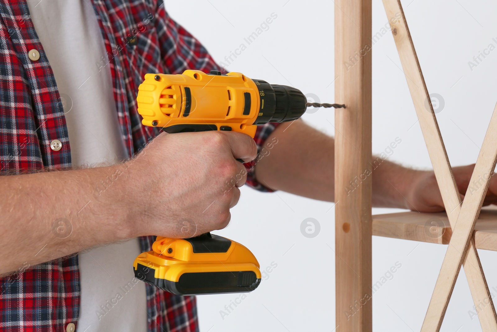 Photo of Man with electric screwdriver assembling furniture indoors, closeup