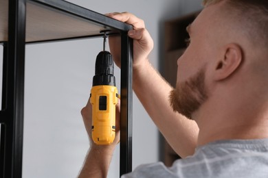 Photo of Man with electric screwdriver assembling furniture indoors, closeup